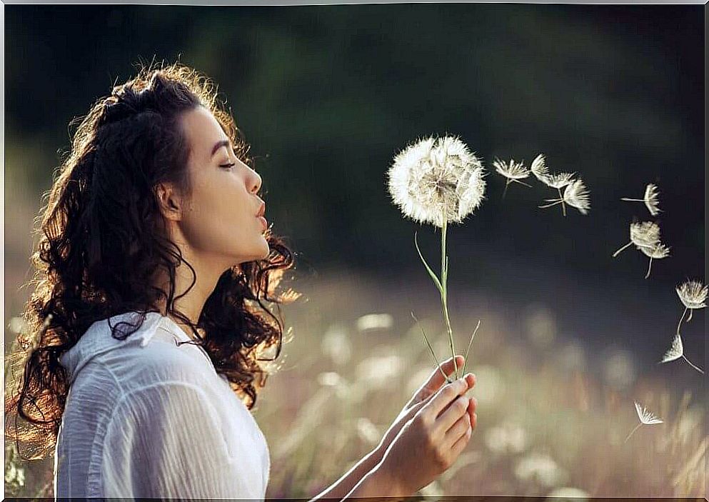 A woman blowing on a dandelion. 